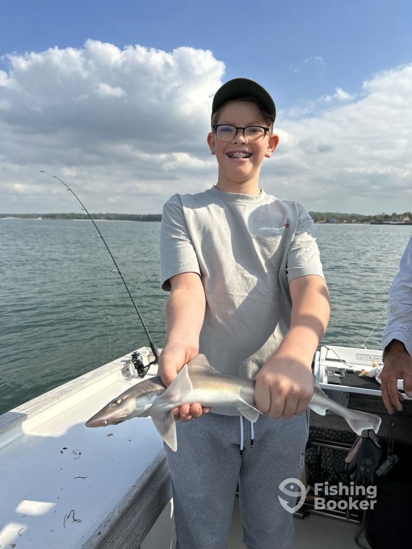 A young angler proudly displaying a small shark while fishing on a boat, enjoying a day on the water.