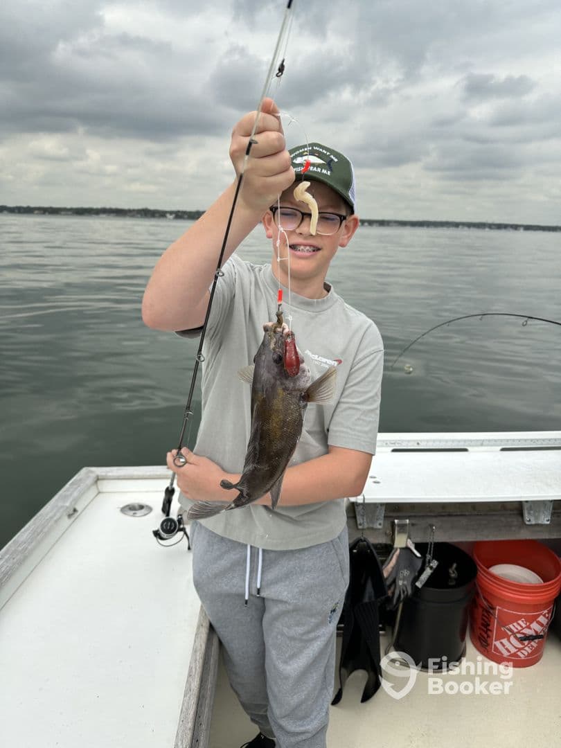 Young angler proudly holding a fish while fishing on a boat, showcasing a successful catch during a day on the water.