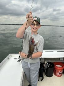 Young angler proudly holding a fish while fishing on a boat, showcasing a successful catch during a day on the water.
