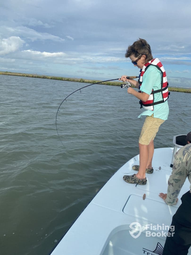 A young angler actively reeling in a fish while fishing from a boat in a coastal environment, showcasing excitement and skill.