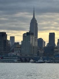 A scenic view of the New York City skyline featuring the Empire State Building, with boats docked along the waterfront.