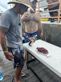 Two anglers at the dock preparing to enjoy freshly caught fish, showcasing a plate of fish fillets.