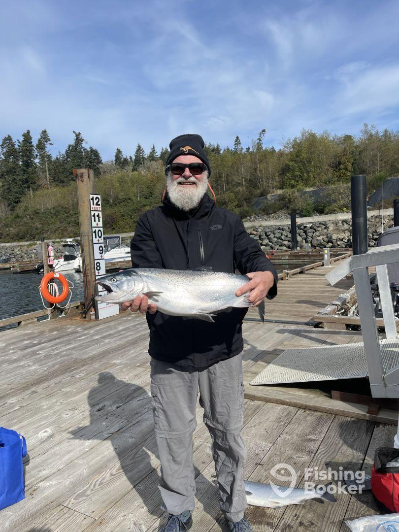 An angler proudly displaying a large Salmon at the dock, showcasing a successful fishing trip in a scenic environment.