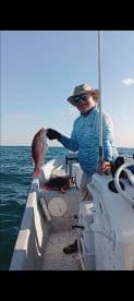 An angler proudly displaying a Red Snapper while fishing on a small boat in open waters.