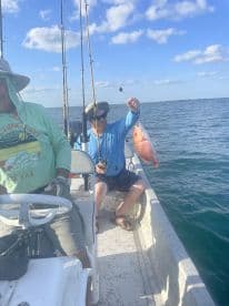 Angler reeling in a vibrant Red Snapper while fishing on a sunny day in open waters.