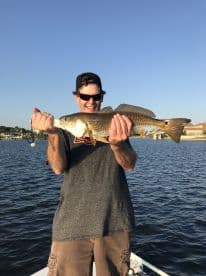 Angler proudly displaying a large Redfish while fishing from a boat in a calm water setting.