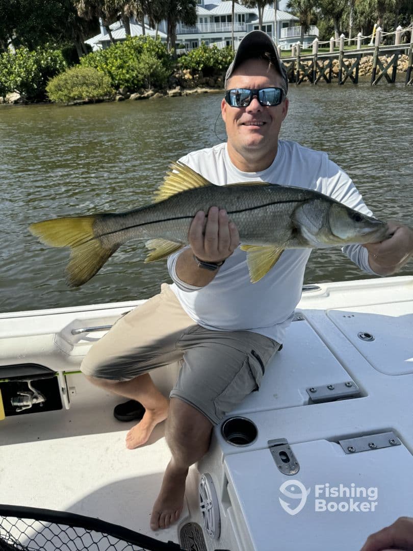 An angler proudly displaying a Snook caught while fishing from a boat in a scenic coastal environment.