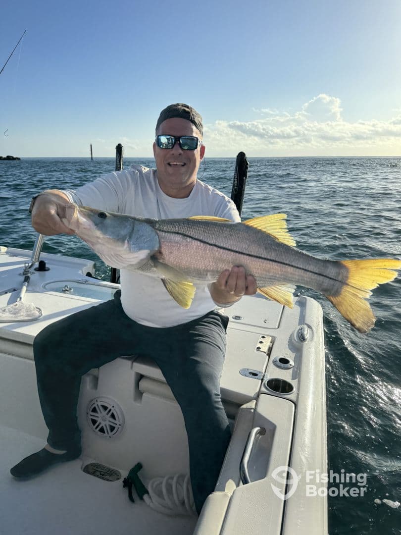 Angler proudly displaying a large Snook while fishing from a boat in clear waters.