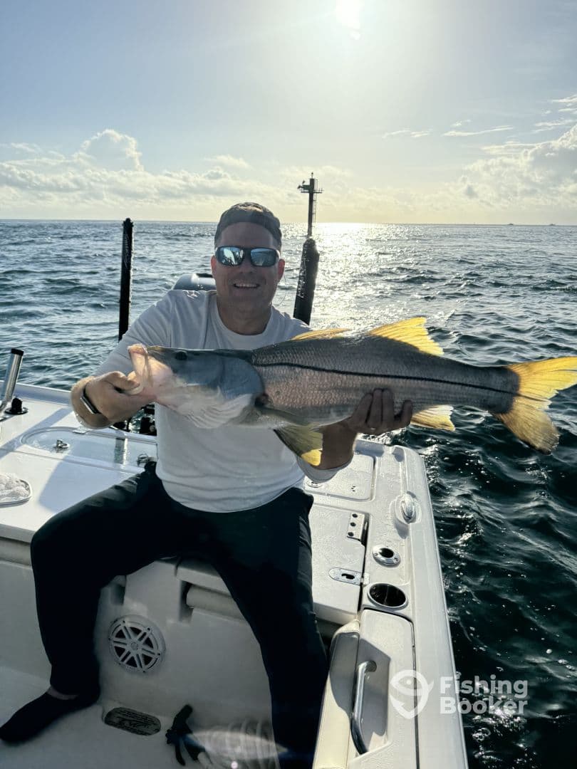 Angler proudly displaying a large Snook while fishing on a boat in open waters.