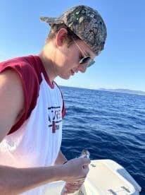 A young angler is focused on reeling in a fish while fishing on a boat in open waters.