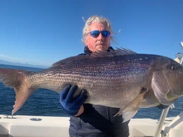 Angler proudly displaying a large Snapper while fishing on a clear day, showcasing the beautiful ocean backdrop.