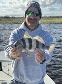 An angler proudly displaying a Sheepshead caught while fishing in a scenic waterway, showcasing the beautiful natural surroundings.