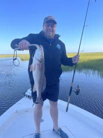 An angler proudly displaying a large Redfish while fishing from a boat in a scenic coastal environment.