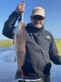 An angler proudly displaying a large Redfish caught in a scenic coastal environment.