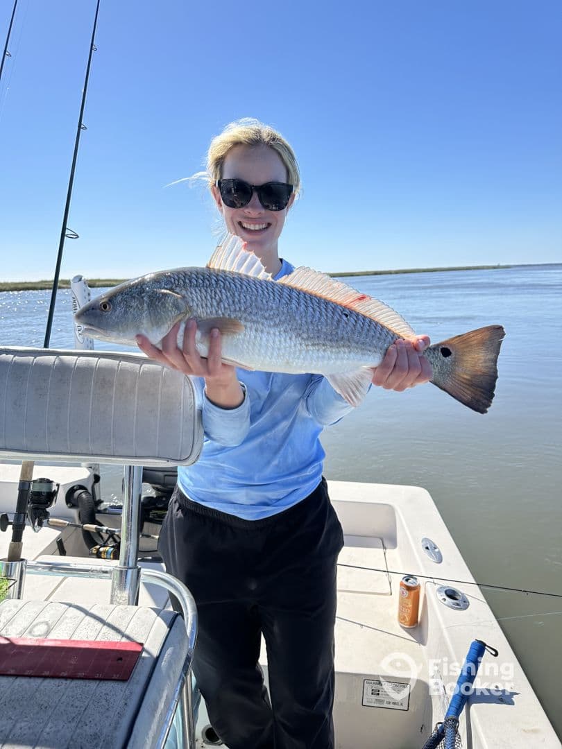 An angler proudly displaying a large Redfish while on a boat, showcasing a beautiful day on the water.