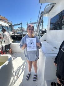 A young angler proudly displaying her fishing tournament certificate for a 34-pound Bass caught during a fishing rodeo, with a scenic marina backdrop.