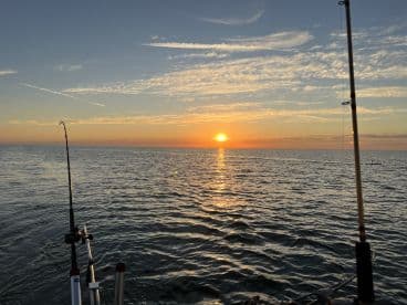 A serene sunset view over the ocean with fishing rods visible, capturing the tranquil atmosphere of a fishing trip.