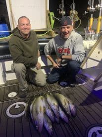 Two anglers proudly displaying their catch of Walleye on the deck of a fishing boat at night.