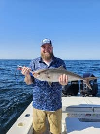 An angler proudly displaying a large Amberjack while fishing offshore, showcasing a beautiful day on the water.