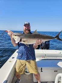Angler proudly displaying a large Amberjack while fishing offshore, showcasing a vibrant blue sky and calm waters.