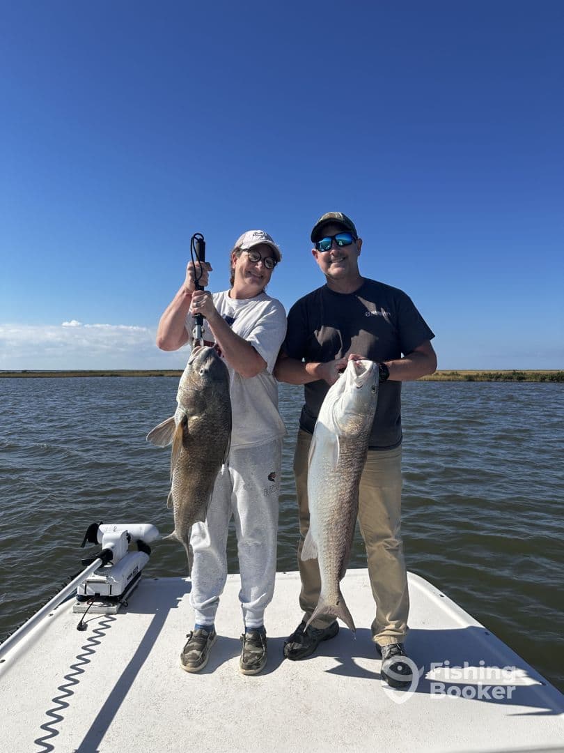 Two anglers proudly displaying their catch of large fish while on a boat in a calm fishing environment.