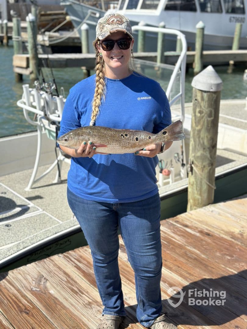 Angler proudly displaying a Speckled Trout at the dock, showcasing a successful day of fishing.