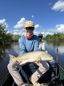 A young angler proudly displaying a Redfish while fishing in a scenic mangrove area.