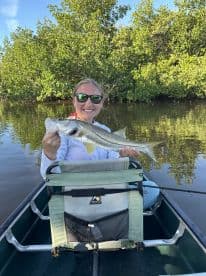An angler proudly displaying a large Snook while kayaking in a serene mangrove setting.