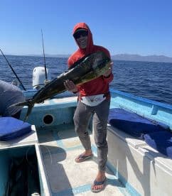 Angler proudly displaying a large Mahi Mahi aboard a fishing boat in clear blue waters.