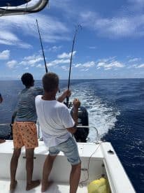 Two anglers actively reeling in their lines while fishing on a boat in open waters, showcasing the excitement of deep-sea fishing.