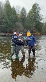 A group of anglers proudly displaying a large fish while wading in a river surrounded by autumn foliage.