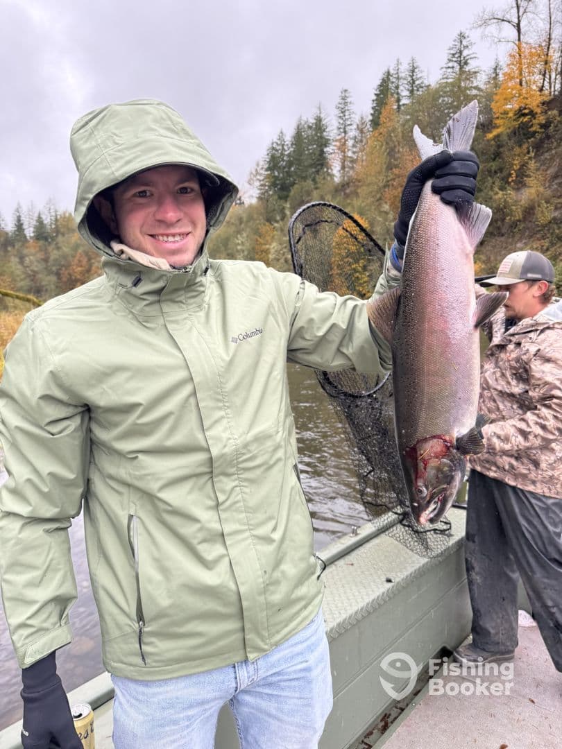 An angler proudly displaying a large Steelhead caught during a river fishing trip, surrounded by autumn foliage.