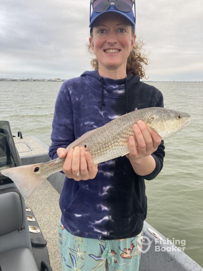 A proud angler holding a freshly caught Redfish while on a fishing trip in a bay environment.