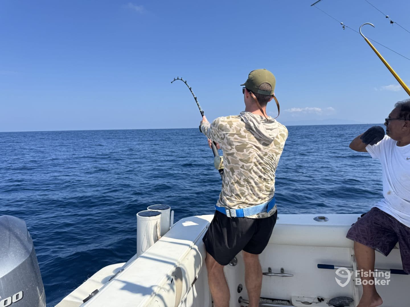 A focused angler reeling in a fish while fishing on a boat in open water, showcasing the excitement of the catch.