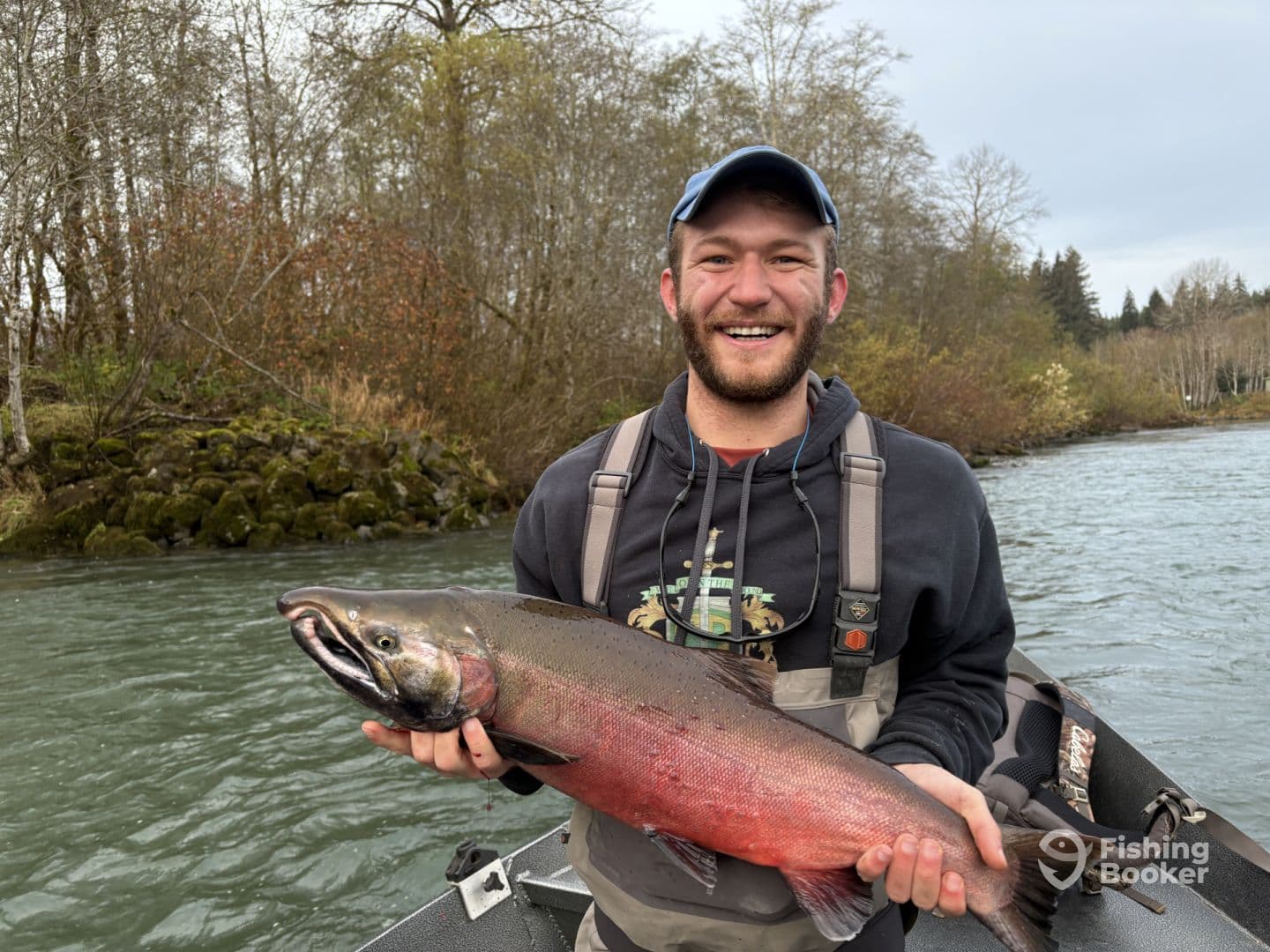 An enthusiastic angler proudly displaying a vibrant Chinook Salmon while fishing in a scenic river environment.