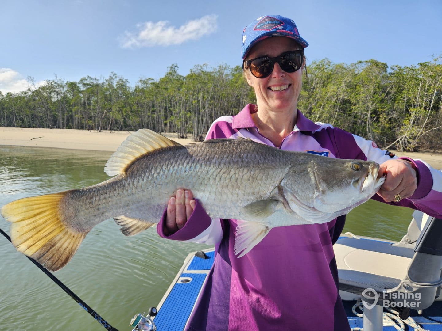 An angler proudly displaying a large Barramundi while fishing in a serene coastal environment.