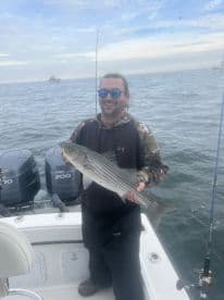 Angler proudly displaying a striped bass while fishing on a boat, showcasing a successful day on the water.