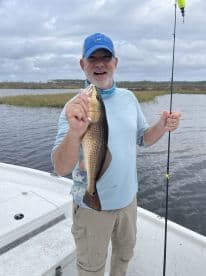 An angler proudly displaying a Redfish while fishing in a scenic coastal environment.