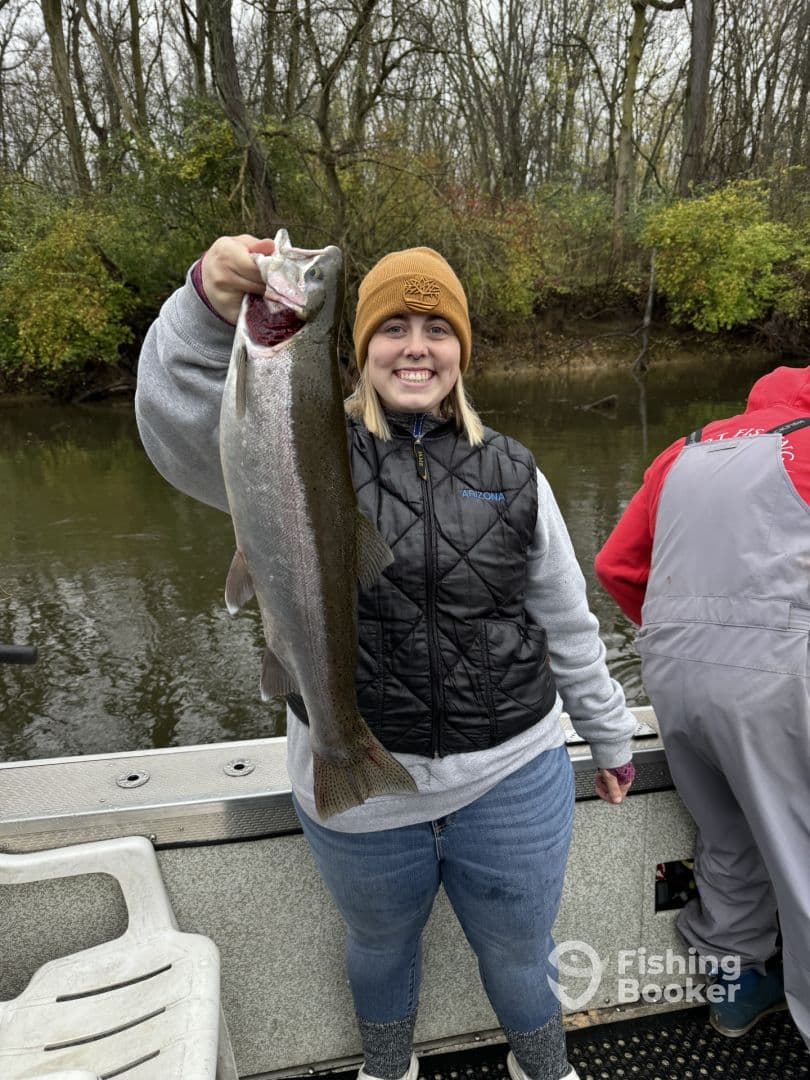 A young angler proudly displaying a large Rainbow Trout while fishing on a river, showcasing the excitement of a successful catch.