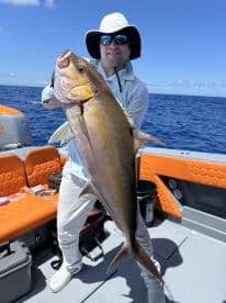 An angler proudly displaying a large Amberjack while fishing on a vibrant boat in open waters.