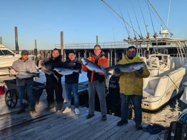 A group of anglers proudly displaying their catch of striped bass at the dock, showcasing a successful fishing trip.
