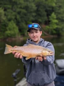 A young angler proudly displaying a large Brown Trout while fishing in a serene freshwater environment.