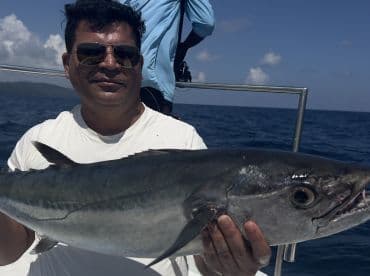 Angler proudly displaying a large fish while fishing offshore, with a scenic ocean backdrop.