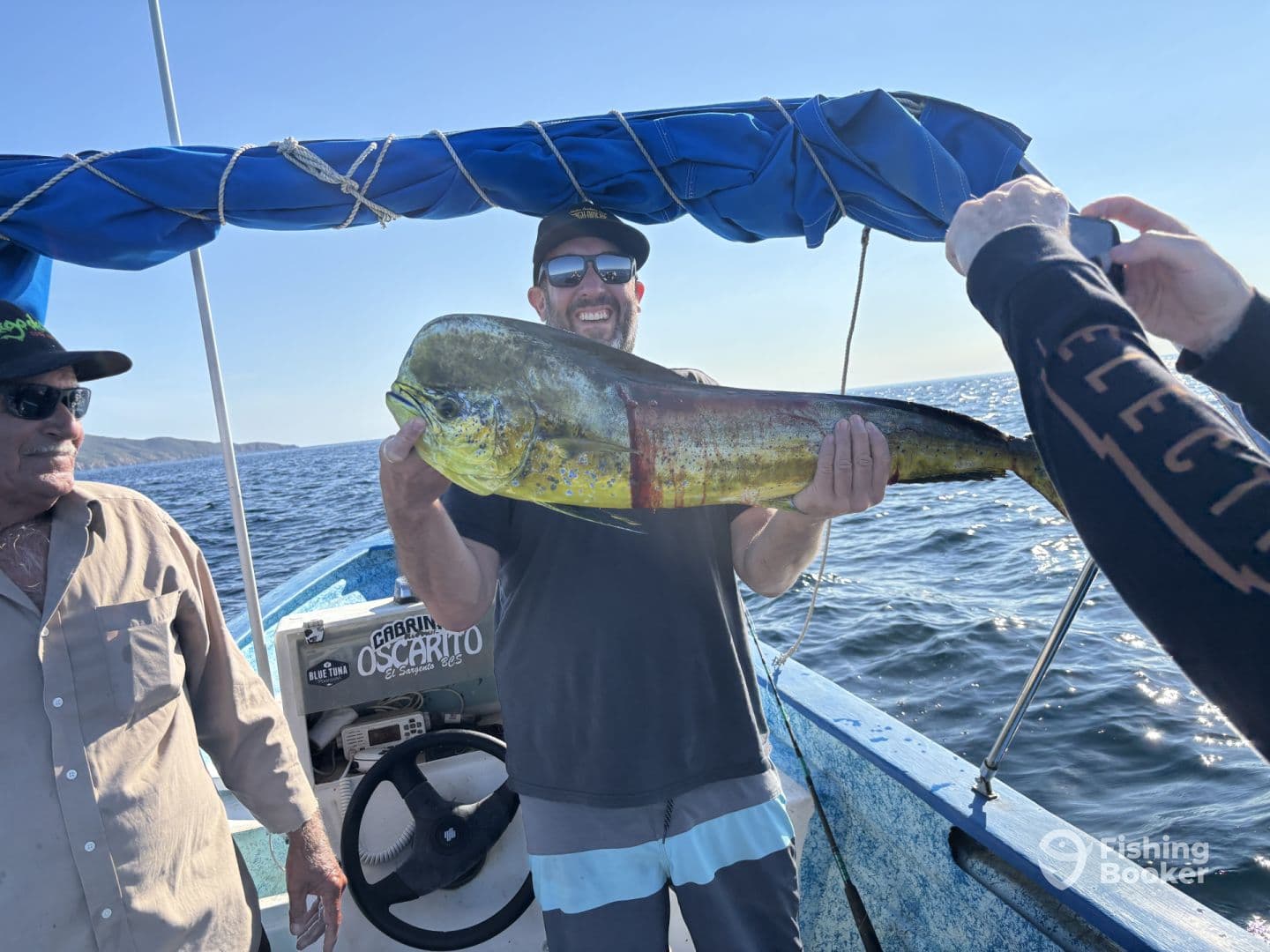 Angler proudly displaying a vibrant Mahi Mahi aboard a fishing boat, with a scenic ocean backdrop.