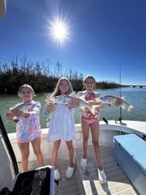 Three young anglers proudly displaying their catch of Snook while enjoying a sunny day on the water.