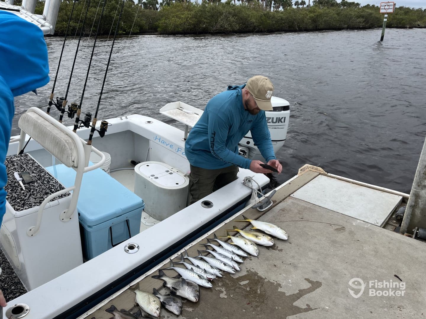 A fisherman is preparing to take a photo of a neatly arranged catch of various fish on the side of a boat, showcasing a successful day on the water.