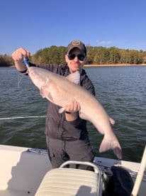 An angler proudly displaying a large Catfish while fishing on a serene lake, showcasing a successful day on the water.