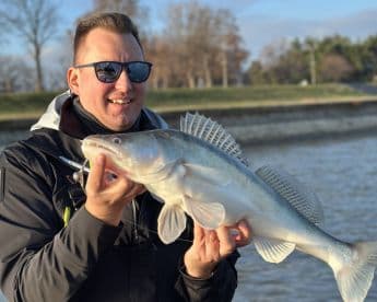 A proud angler displaying a large Zander caught during a fishing trip on a calm river.