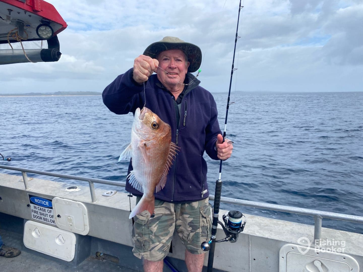 An angler proudly displaying a Snapper while fishing on a boat in open waters.