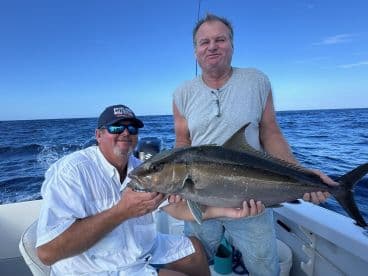 Two anglers proudly displaying a large Amberjack on a fishing boat in open waters.